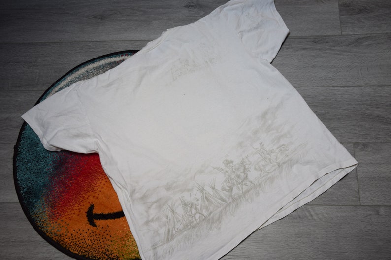 May include: White t-shirt with a gray graphic print of a group of people in a field. The graphic is on the back of the shirt.