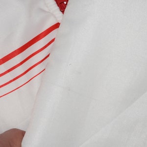 May include: White jacket with red stripes. The jacket is made of a shiny, smooth fabric.