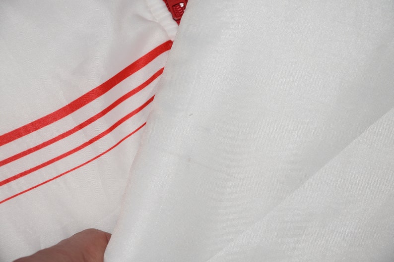 May include: White jacket with red stripes. The jacket is made of a shiny, smooth fabric.