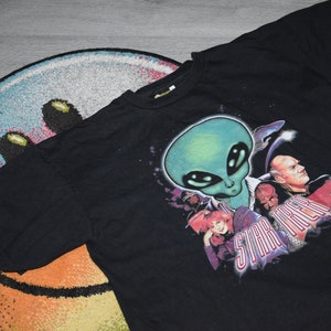 May include: Black t-shirt featuring a graphic print of an alien and characters from Star Trek. The text "Star Trek" is printed on the shirt.