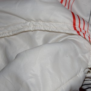 May include: White jacket with red and black stripes. The jacket has a zipper and a drawstring hood.