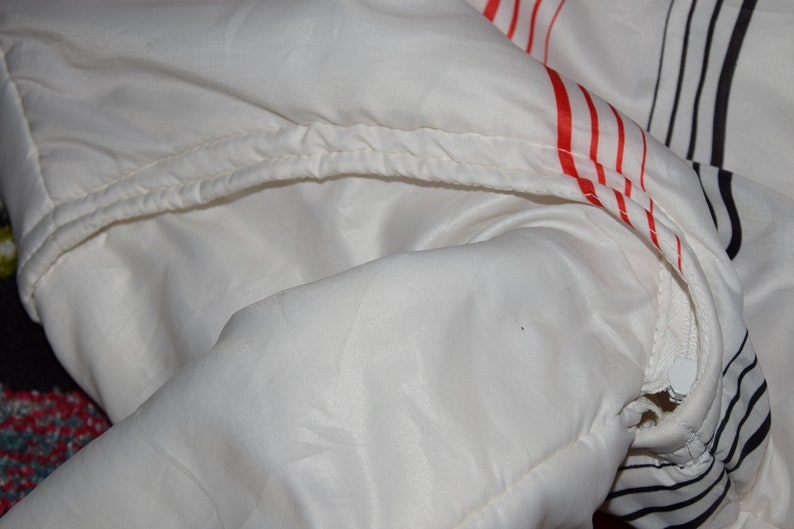 May include: White jacket with red and black stripes. The jacket has a zipper and a drawstring hood.