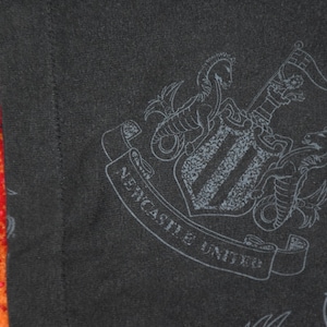 K&ouml;nnte beinhalten: Schwarz-wei&szlig;es Grafikdruck des Wappens des Fu&szlig;ballvereins Newcastle United. Das Wappen zeigt einen Schild mit drei vertikalen Streifen, zwei Seepferdchen und ein Banner mit der Aufschrift "Newcastle United".