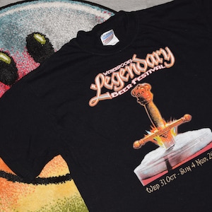 May include: Black t-shirt with a graphic of a sword in a book. The text "Wetherspoons Legendary Beer Festival" and "Wed 31 Oct - Sun 4 Nov, 2001" are printed on the shirt.