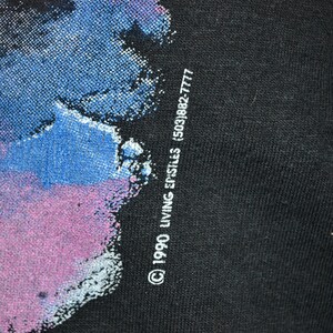 Może przedstawiać: Czarny t-shirt z kolorowym abstrakcyjnym wzorem w odcieniach niebieskiego, fioletowego i białego. Tekst "&copy; 1990 LIVING EPISTLES (503)882-7777" jest wydrukowany na dole po prawej stronie.