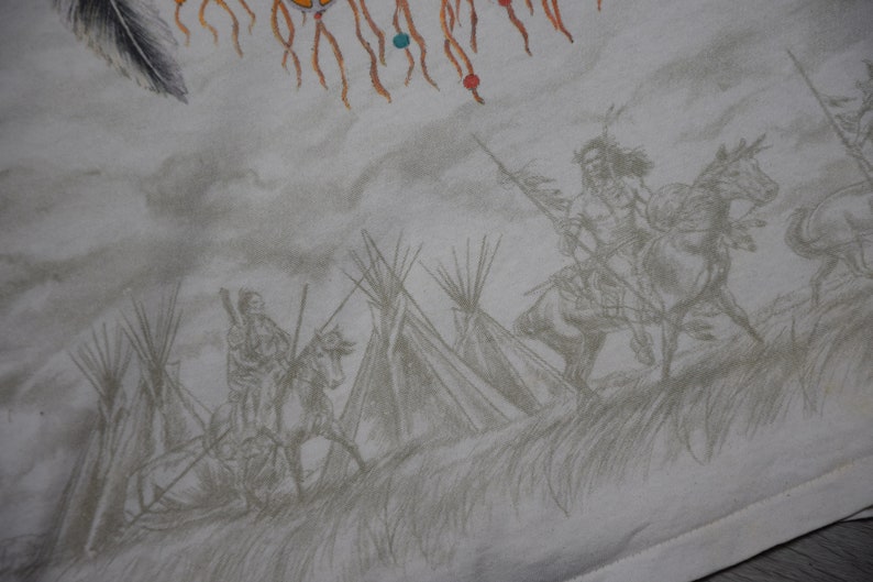 May include: A white t-shirt with a Native American design. The design features a dreamcatcher, tipis, and Native American figures on horseback.