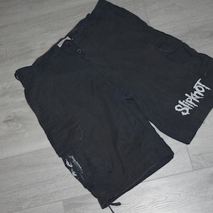 Op de afbeelding: Zwarte cargoshorts met witte "Slipknot" letters op het rechterbeen. De shorts hebben meerdere zakken en trekkoordverstellingen. De shorts zijn gemaakt van een duurzame stof.