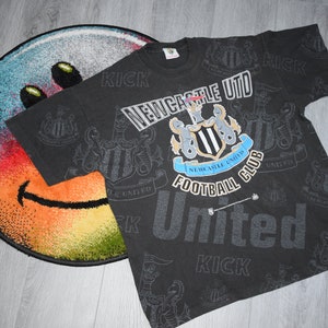 K&ouml;nnte beinhalten: Schwarzes T-Shirt mit einem sich wiederholenden Muster des Logos des Newcastle United Football Club und den Worten "Kick" und "United".