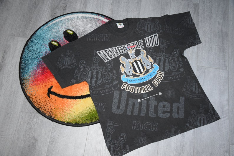 K&ouml;nnte beinhalten: Schwarzes T-Shirt mit einem sich wiederholenden Muster des Logos des Newcastle United Football Club und den Worten "Kick" und "United".