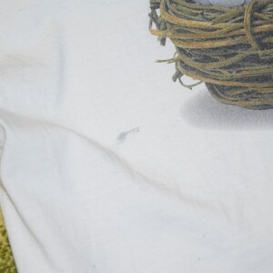 May include: White t-shirt with a brown and green nest printed on the top right corner.