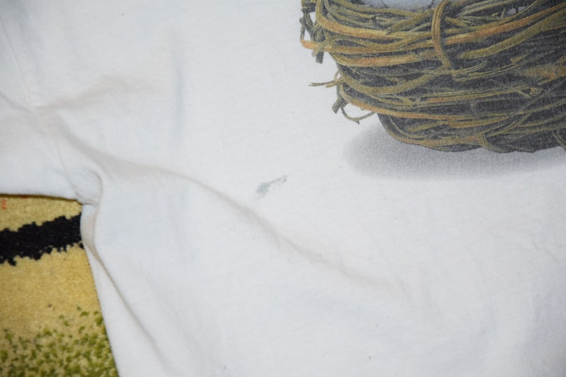 May include: White t-shirt with a brown and green nest printed on the top right corner.