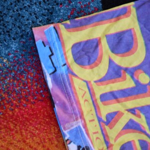Puede incluir: Una camiseta morada y amarilla con la palabra "Bike" impresa en ella en una fuente grande y en negrita. La palabra "Action" est&aacute; impresa debajo de la palabra "Bike" en una fuente m&aacute;s peque&ntilde;a.