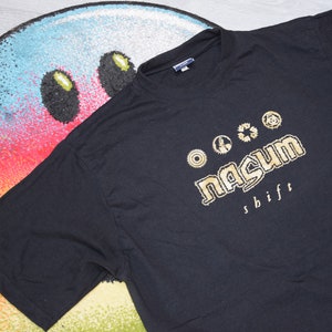 May include: Black t-shirt with a gold graphic of the band Nasum. The graphic includes the band's name and the words "shift".