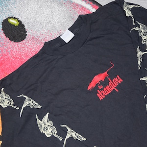 Puede incluir: Camiseta negra de manga larga con un gráfico de rata roja y el texto "the stranglers". Las mangas tienen un diseño repetido de pájaros blancos. La camiseta está hecha de un material suave.