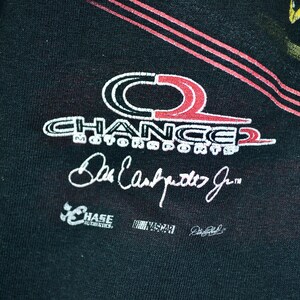 Op de afbeelding: Zwart t-shirt met het Chance 2 Motorsports logo in wit en rood, en de handtekening van Dale Earnhardt Jr. Het shirt toont ook de logo's van Chase Authentics en NASCAR.