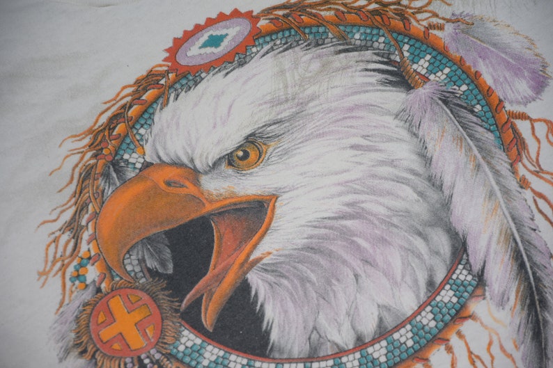 May include: A white bald eagle with a bright orange beak and yellow eyes is depicted in a Native American headdress. The headdress is made of feathers, beads, and a beaded band with turquoise and orange accents.