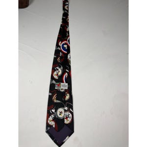 May include: A black necktie featuring a repeating pattern of Mickey Mouse characters, circular clock faces, and red, white, and blue shield motifs. A rectangular white label is stitched to the center, displaying the Disney logo and text.