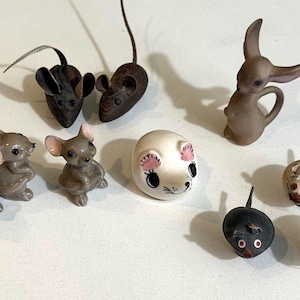 May include: A collection of eleven small animal figurines including several grey mice, two dark brown mice with long tails, a light brown rabbit-like figure, a round white mouse head with pink ears, and two small round mice with dark and light bodies.