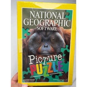 May include: A rectangular National Geographic Software Picture Puzzle box with a bright yellow border. The front features a large orangutan portrait set against a green jigsaw puzzle pattern. Text includes National Geographic Software and Picture Puzzle.