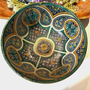 May include: A decorative ceramic bowl with an intricate, colorful pattern. The bowl features a teal rim and a detailed design in shades of blue, green, yellow, and white. The bowl is round and appears to be handmade.