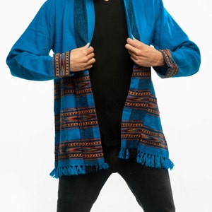 Male model wearing a turquoise cardigan with brown accents and fringe on the ends.
