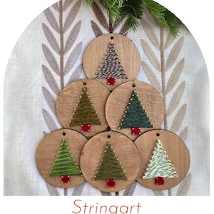 May include: Six circular wooden ornaments arranged in a tree shape, each featuring string art of a Christmas tree. The trees are created with various shades of green and white thread, metallic pins, and a small red square base at the bottom.