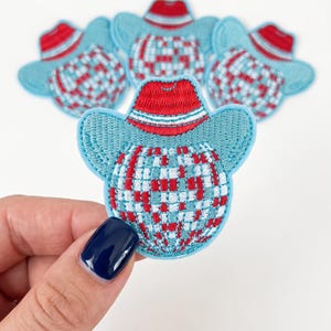 May include: A group of embroidered patches featuring a disco ball design topped with a red cowboy hat. The disco ball is rendered in a checkered pattern of light blue, white, and red thread, while the hat has a red crown and light blue brim.