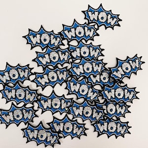 May include: A pile of blue and white iron-on patches with the word "WOW" in a white, sparkly font. The patches are shaped like a comic book speech bubble.