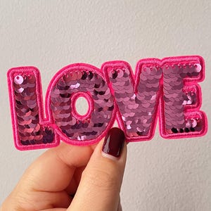 May include: Pink felt patch with the word "LOVE" in pink sequins. The patch is sewn with a pink thread.