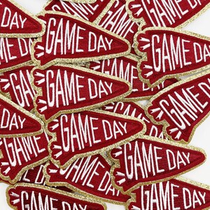 May include: A pile of red felt pennants with gold glitter trim and white embroidery that reads "GAME DAY".