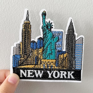 May include: Embroidered patch featuring the New York City skyline, including the Statue of Liberty, the Empire State Building, and other skyscrapers. The patch has a white border and the words "NEW YORK" in white lettering on a black background.