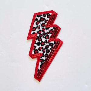 May include: Red and black lightning bolt shaped patch with a leopard print design and red sequins around the edges.