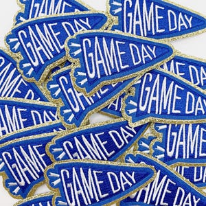 May include: A pile of blue and gold felt pennant patches with the text "GAME DAY" embroidered in white.