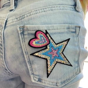 May include: Light blue denim jeans with a sparkly star and heart patch on the back pocket.