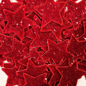 May include: A pile of red sequined star-shaped patches. The stars are made of a soft, velvety material and are covered in sparkling sequins.