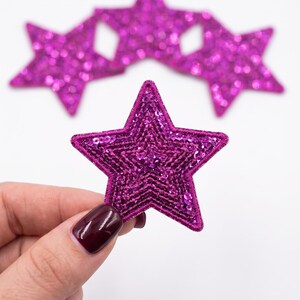 May include: Four star-shaped patches in a vibrant magenta color. Each patch features a dense, textured surface covered in small, reflective sequins that catch the light. The edges of each star are finished with a matching magenta stitched border.