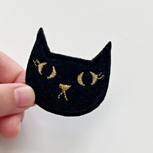 May include: Black felt cat patch with gold embroidered eyes and nose.