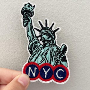 May include: Embroidered patch featuring the Statue of Liberty in shades of blue and black. The patch includes the letters "NYC" in white on a red and blue background. The patch is on a white background.