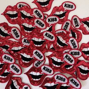 May include: A pile of red sequin lips with a white speech bubble that says "KISS" on each one.