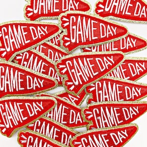 May include: A pile of red felt pennant patches with gold glitter trim. Each patch has the text "GAME DAY" in white lettering.