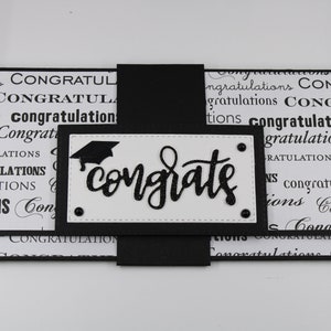 Pu&ograve; includere: Un biglietto di laurea bianco e nero con un cappello di laurea nero e la parola "congrate" in corsivo nero. Il biglietto &egrave; decorato con un motivo bianco e nero della parola "congratulazioni".
