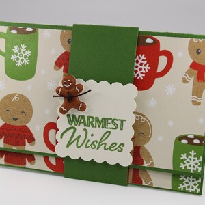 May include: A green and brown Christmas card with a gingerbread man and a mug of hot chocolate. The card has the words "Warmest Wishes" on it.