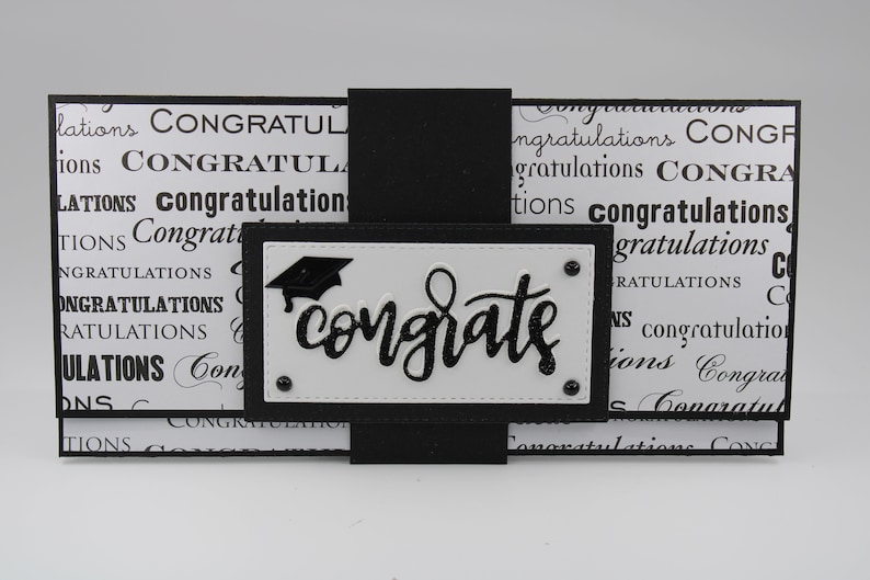 Pu&ograve; includere: Biglietto di laurea bianco e nero con un cappello di laurea nero e la parola "congrats" in lettere glitter nere.