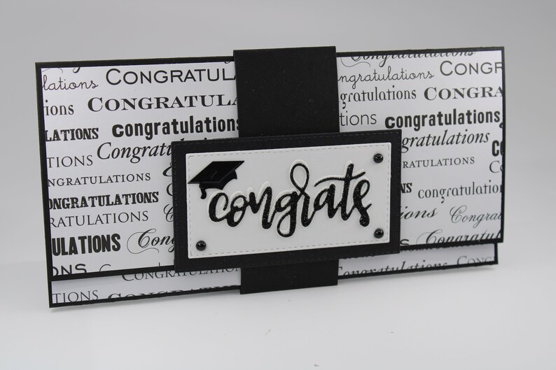Pu&ograve; includere: Biglietto di laurea bianco e nero con un cappello di laurea nero e la parola "congrats" in lettere glitter nere.