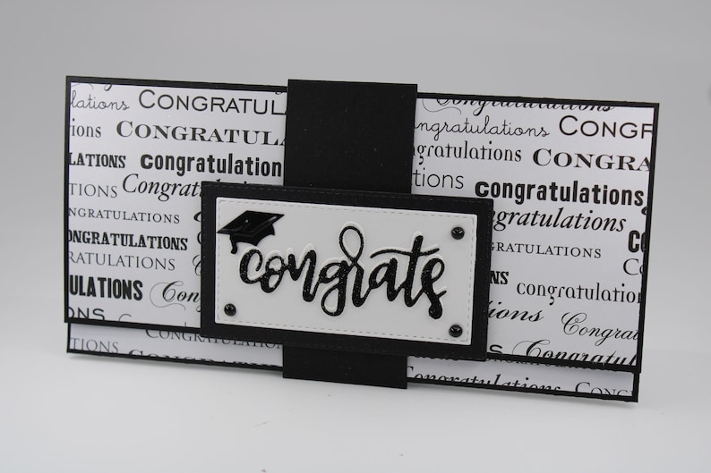 Pu&ograve; includere: Biglietto di laurea bianco e nero con un cappello di laurea nero e la parola "congrats" in lettere glitter nere.
