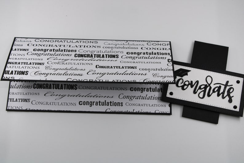 Pu&ograve; includere: Biglietto di laurea bianco e nero con la parola "congrate" scritta in corsivo. Il biglietto &egrave; decorato con un cappello di laurea e ha uno sfondo nero.