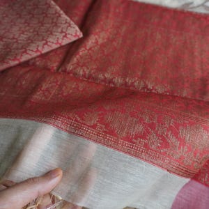 May include: Close-up of a red and gold patterned textile with a matching square piece. The fabric has a detailed floral design and a contrasting white border. The textile is folded, showing its texture and color variations.