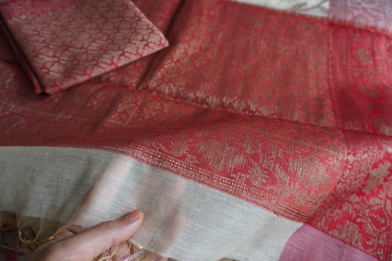May include: Close-up of a red and gold patterned textile with a matching square piece. The fabric has a detailed floral design and a contrasting white border. The textile is folded, showing its texture and color variations.