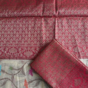 May include: A red and gold patterned textile with a matching folded piece. The fabric features intricate floral and geometric designs. The bottom portion of the textile has a white background with colorful floral and leaf patterns.