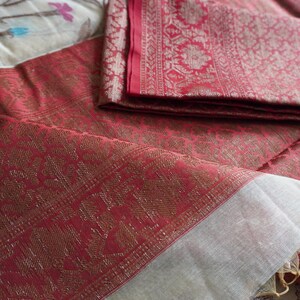 May include: A folded red textile with a gold floral pattern and a white border. The fabric is layered on top of a floral patterned surface. The textile has a luxurious appearance.